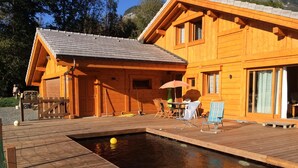 Eine Holzhütte mit Swimmingpool, Liegestühlen und einem Tisch mit Sonnenschirm.