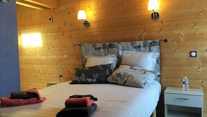 Ein Zimmer mit Holzwänden, einem Bett, zwei Wandleuchten und einem Nachttisch mit einer Flasche.