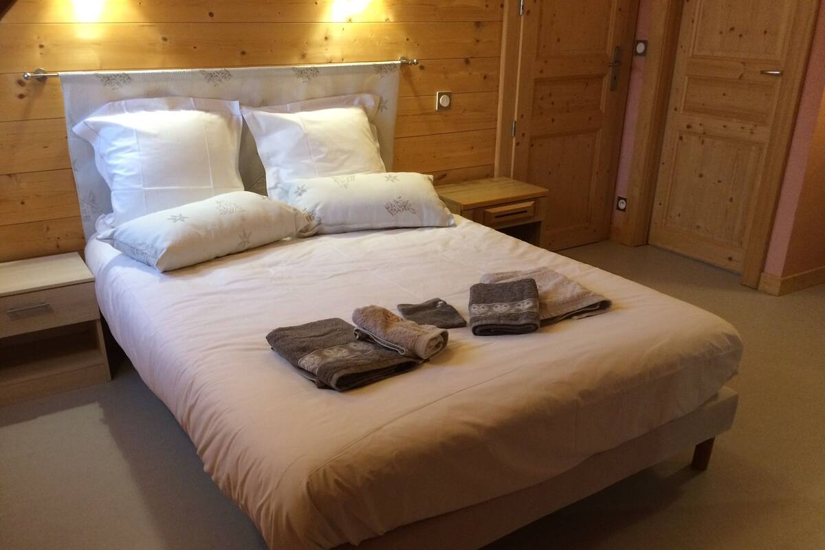 Un lit bien fait, avec une couette blanche, deux oreillers et un ensemble de serviettes posées sur le lit.