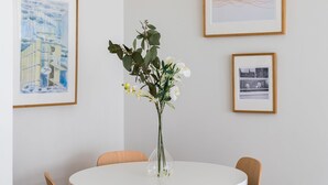 Ein runder, weißer Tisch mit einer Blumenvase und grünen Blättern, umgeben von Holzstühlen.
