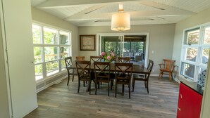Un espace repas avec une table et des chaises en bois, de grandes fenêtres et un ventilateur de plafond.