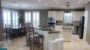 Een moderne keuken met witte kasten, een centraal eiland en een eethoek met houten stoelen.