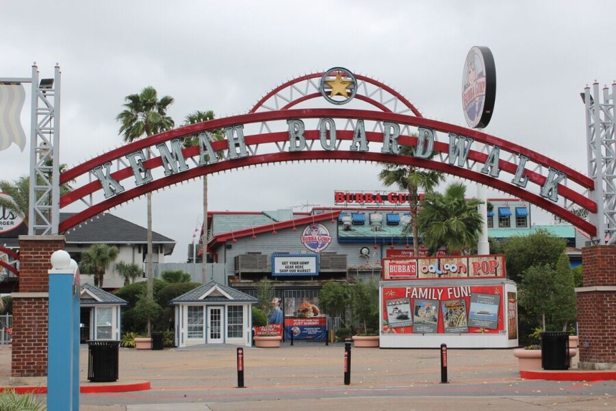 Entrance arch of Kemah Boardwalk near Houston with palm trees, restaurants, and colorful family attraction signs.