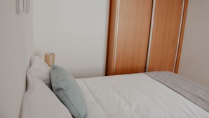 A bedroom with a bed, pillows, a bedside table, and a wooden wardrobe.