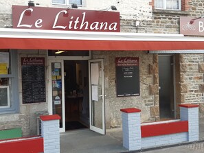 Exterior del hotel restaurante bar Le Lithana con un cartel, menú y fachada de ladrillo.
