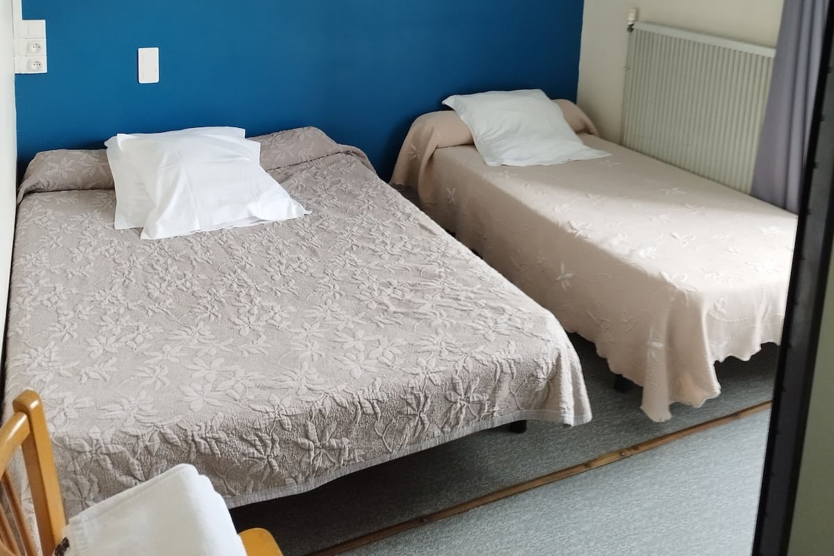 A room with two beds, a blue wall, a radiator, and a ceiling light.