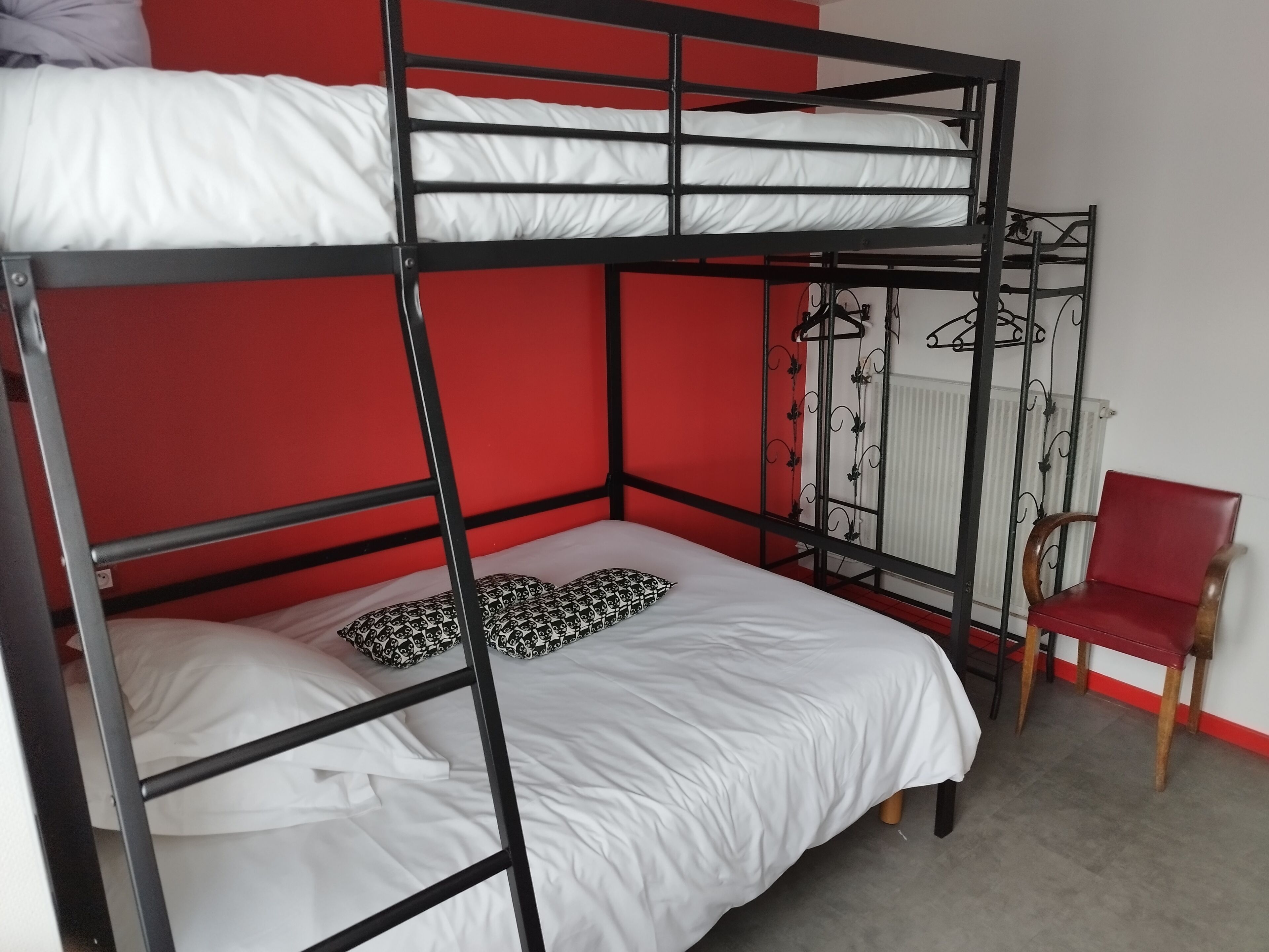 A bunk bed with white bedding and patterned pillows, a red chair, and a radiator in a room with red walls.