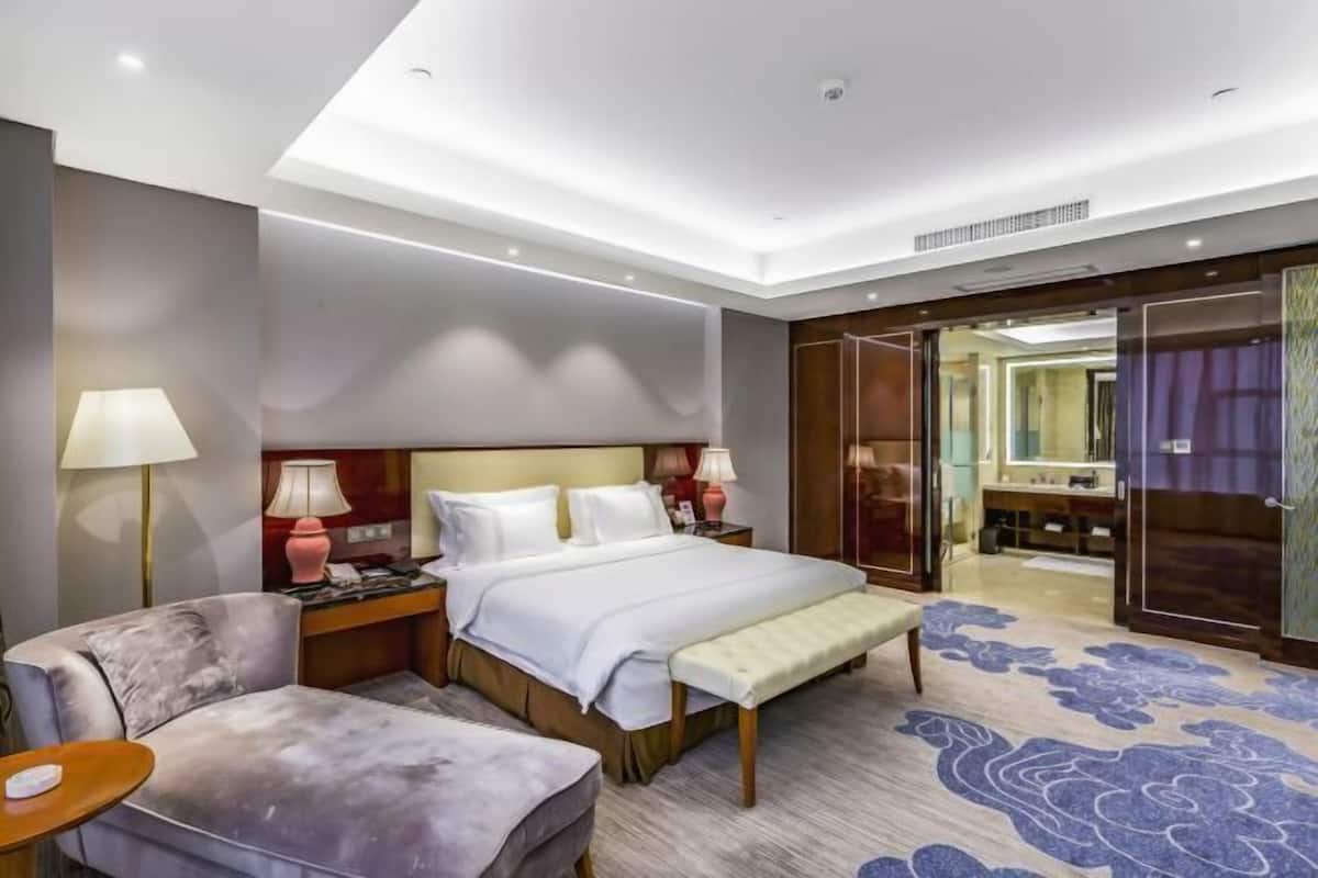 Een hotelkamer met een bed, nachtkastjes, een bankje, een stoel, een bureau, een spiegel en een badkamer die door een open deur zichtbaar is.