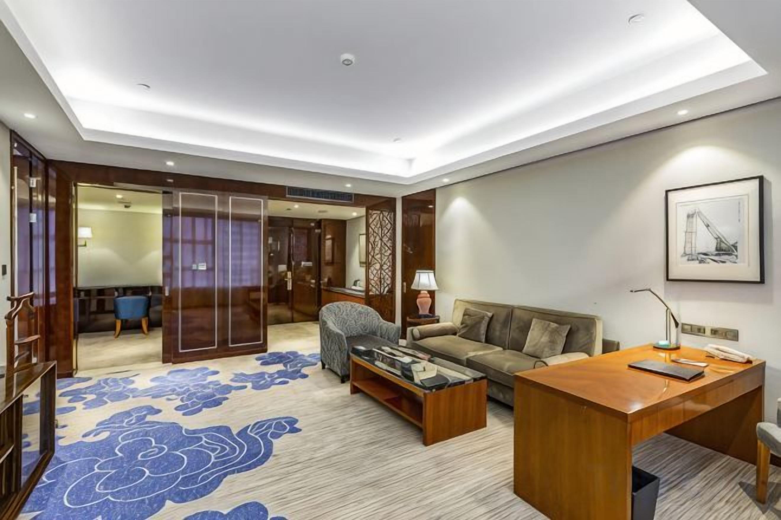 Ein modernes Hotelzimmer mit einem Holztisch, einer Couch, einem Couchtisch und einem gemusterten Teppich.