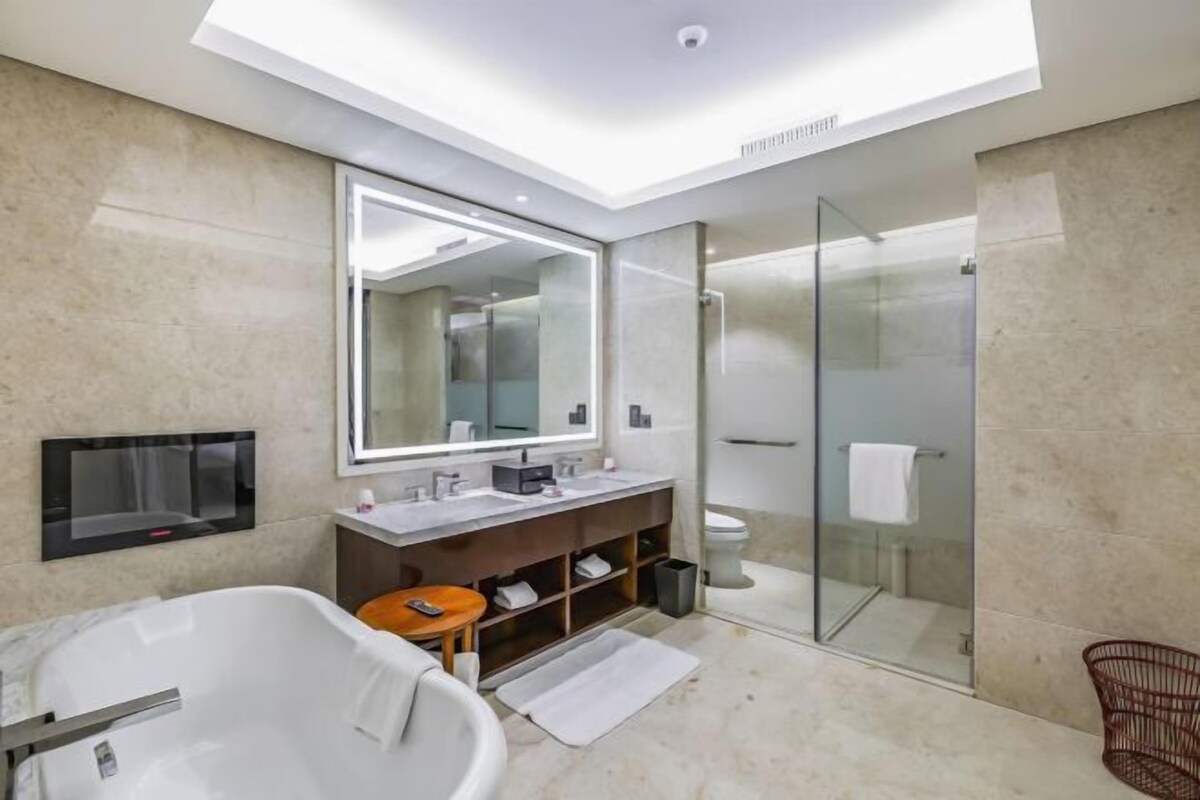 Un baño moderno con una bañera independiente, un espejo grande, un box de ducha de vidrio y un tocador con lavabo y espacio de almacenamiento.