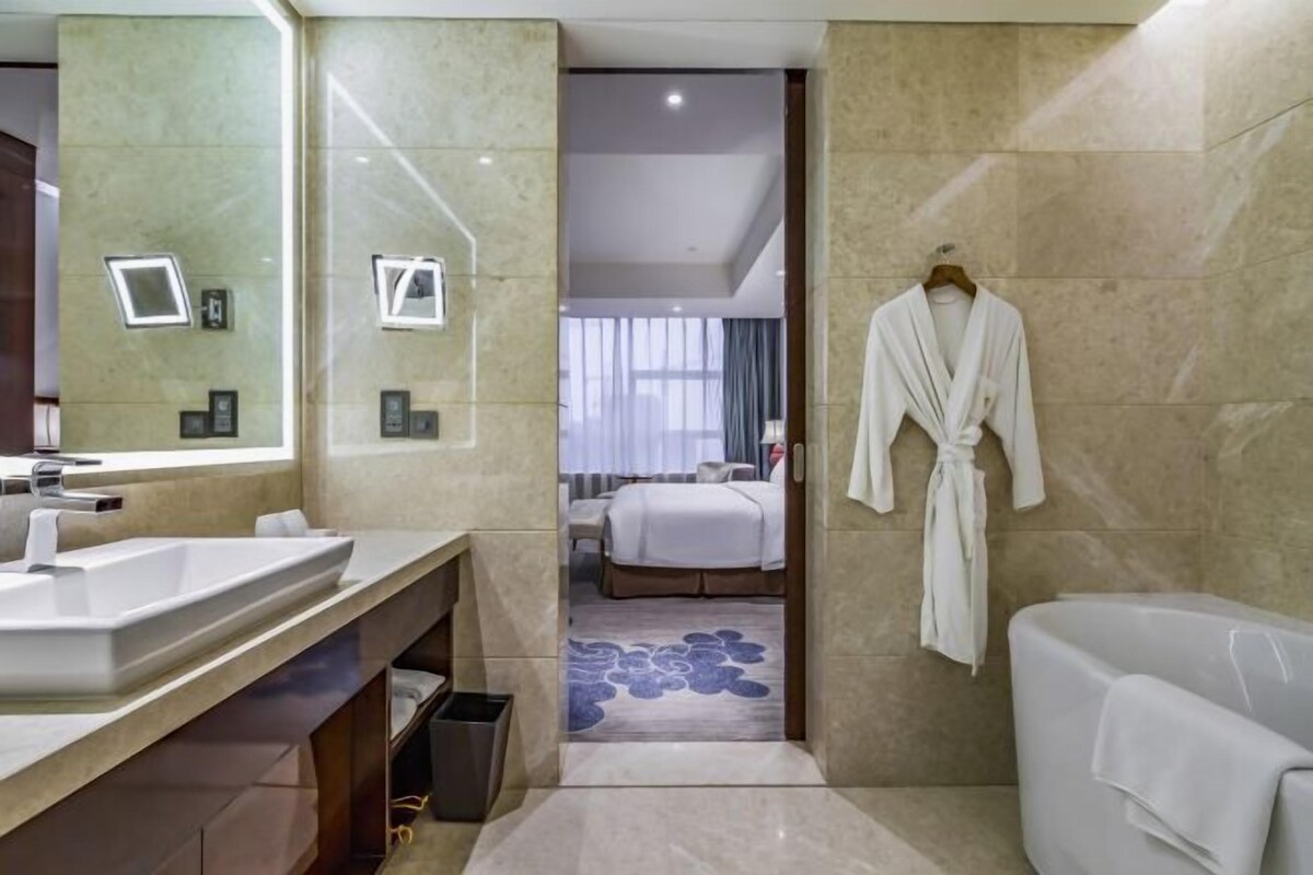 A modern bathroom with a large mirror, a sink, a bathtub, and a robe hanging on the wall.