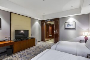 Habitación de hotel con cama, televisión, escritorio, espejo, lámpara y puerta que da a un baño.