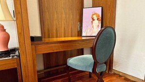 A wooden desk with a framed picture, a teal chair, and a pink vase.