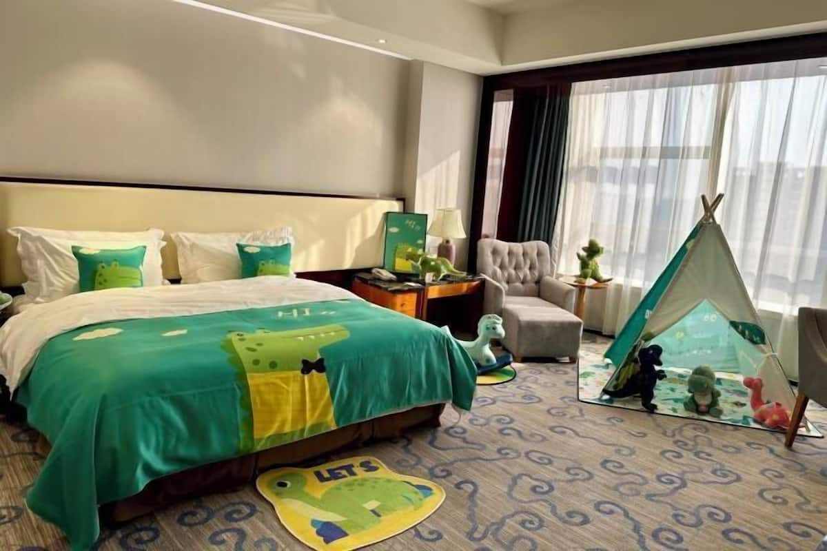 Een hotelkamer met een bed, een stoel, een nachtkastje, een lamp, een raam met gordijnen en een tipi.