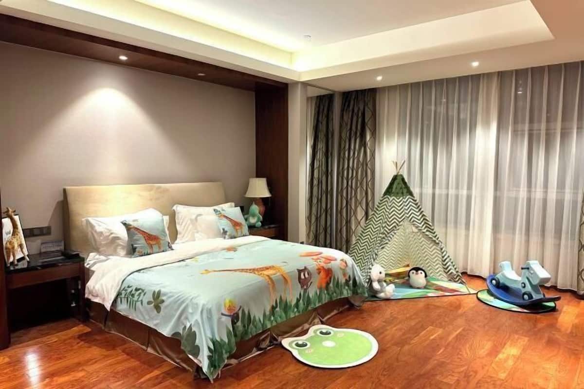Een slaapkamer met een bed, nachtkastje, lamp, gordijnen, een tent en kinderspeelgoed.