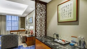 A hotel room with a sofa, a desk, a decorative screen, a framed artwork, and a marble countertop with amenities.