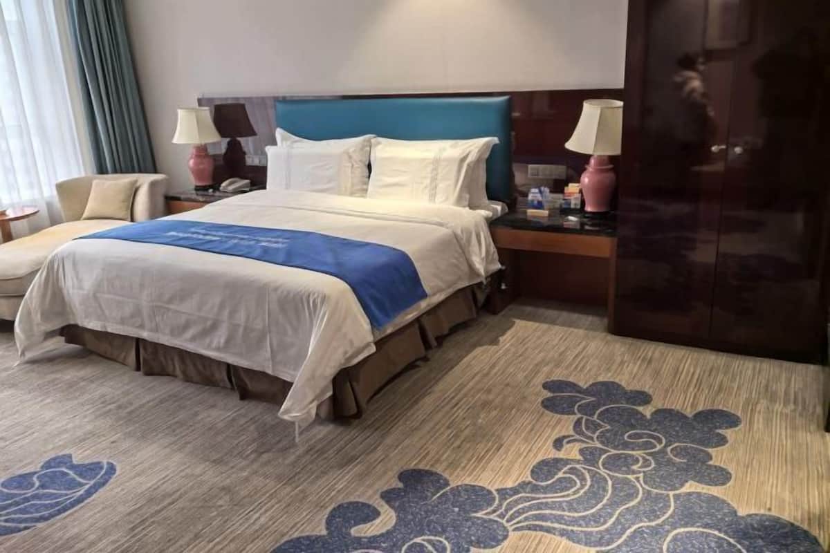 Een hotelkamer met een bed, nachtkastjes, lampen, een stoel en een decoratief vloerkleed.