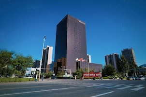 Un edificio alto con fachada oscura, rodeado de otros rascacielos y un cielo azul despejado.