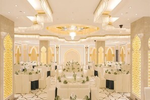 A banquet hall with round tables, chandeliers, and ornate wall decorations. - The Garden Hotel Tangshan (Tangshan)
