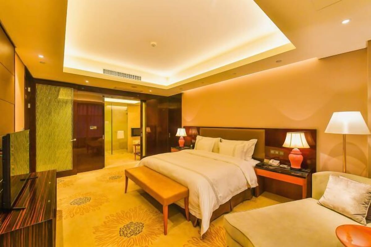 A hotel room with a bed, bedside table, lamp, and a bench.