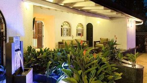 An outdoor seating area with plants and a water feature, a covered entrance, and a building with a white exterior. - Luxury Air Road (Medellín)