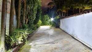 A pathway flanked by lush greenery and a white wall, leading towards a bright light at the end. - Luxury Air Road (Medellín)