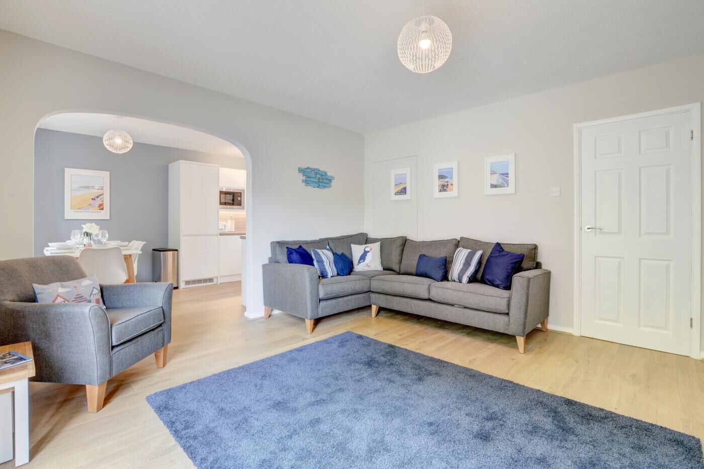 A modern living room with a grey sectional sofa, a blue rug, and a dining area with white furniture.