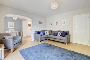 Ein modernes Wohnzimmer mit einem grauen Ecksofa, einem blauen Teppich und einem Essbereich mit weißer Möbel.