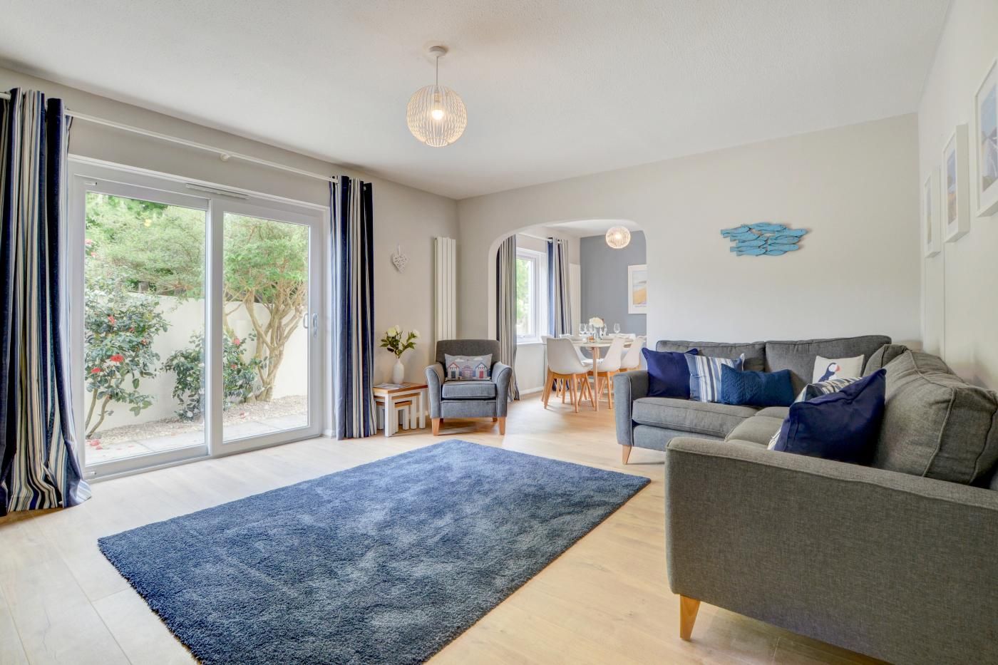 A spacious living room with a grey sofa, a blue rug, and a dining area with a table and chairs.