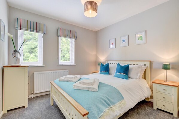 A bedroom with a bed, bedside tables, a radiator, and windows with blinds.
