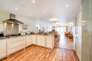 A modern kitchen with a central island, wooden flooring, and a dining area with a sofa and table. - 2 Bed in Mortehoe (oc-schon) (Mortehoe)
