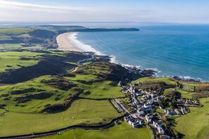 An aerial view of a coastal village with a beach, green fields, and houses.