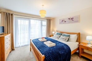 A hotel room with a bed, a TV, a wooden dresser, a nightstand, and a window with curtains.
