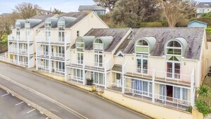 A row of seaside cottages with multiple balconies, a paved road in front, and trees in the background.