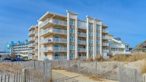 A multi-story hotel with balconies, located near a sandy beach.