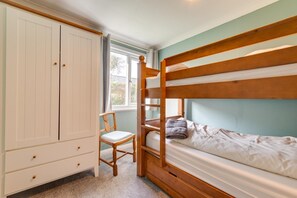 A bunk bed room with a wooden bunk, a chair, a wardrobe, and a window.
