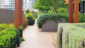 A wooden pathway leading through a lush garden area with dense foliage and a variety of plants.