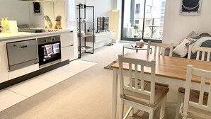 A modern kitchen with a dining area, white cabinetry, and a large window offering a view of the city.