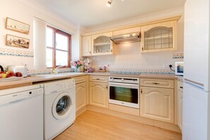 A compact kitchen with a washing machine, oven, and a window with curtains.