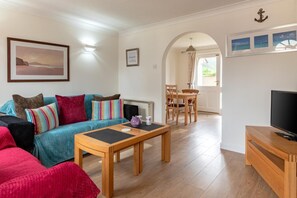 A living room with a sofa, coffee table, TV, and dining area with chairs and a table. - 2 Bed in Croyde (oc-sscape) (Croyde)