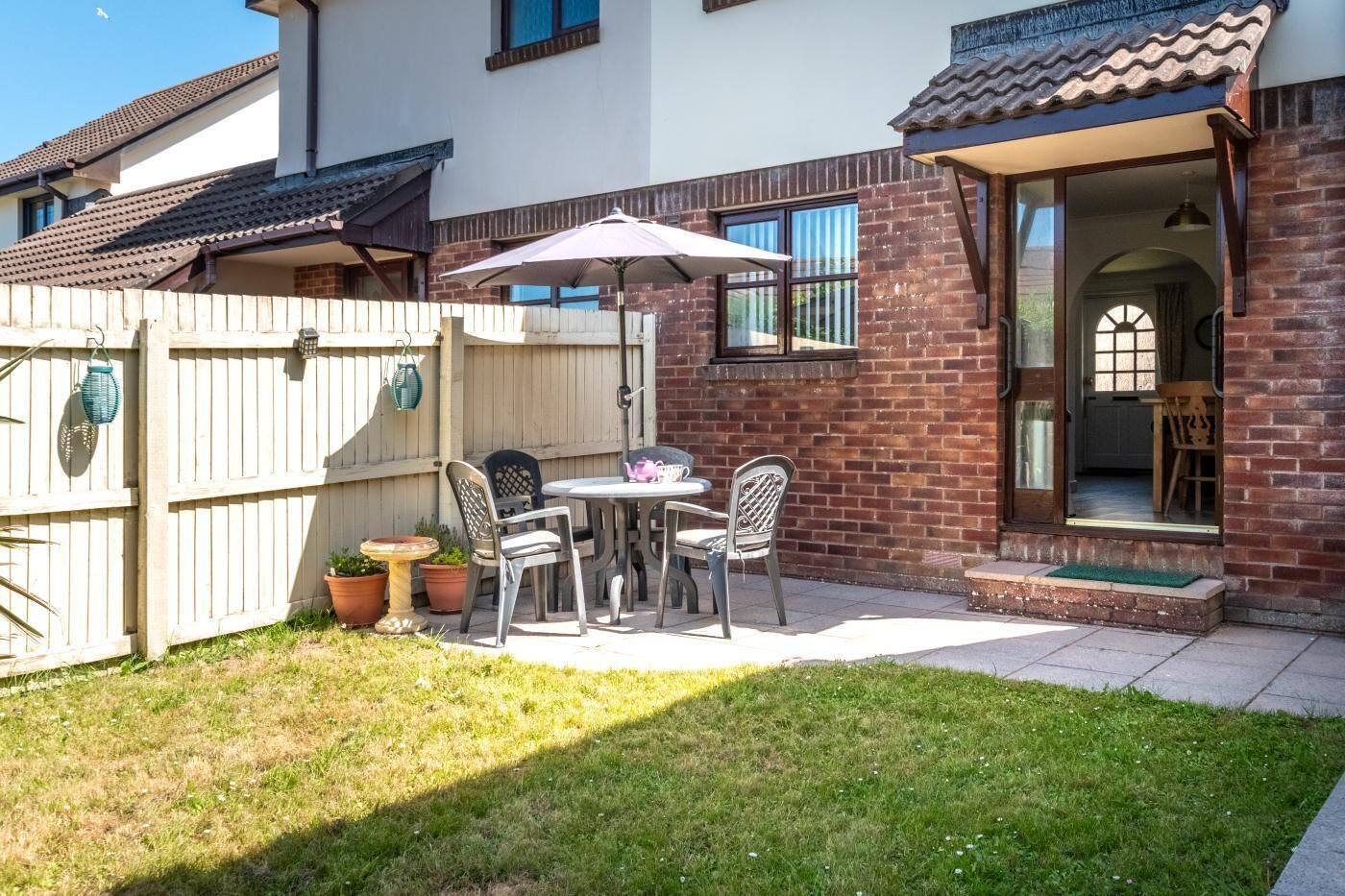 A patio with a table and chairs, a wooden fence, and potted plants.