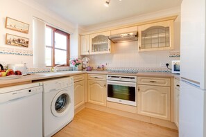 A compact kitchen with a washing machine, oven, and a window with curtains. - 2 Bed in Croyde (oc-sscape) (Croyde)