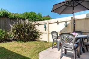 A patio with a table and chairs, a large umbrella, and a wooden fence. - 2 Bed in Croyde (oc-sscape) (Croyde)