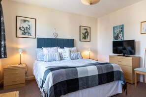 A neatly arranged bedroom with a bed, bedside tables, a TV, and artwork on the walls. - 2 Bed in Croyde (oc-sscape) (Croyde)