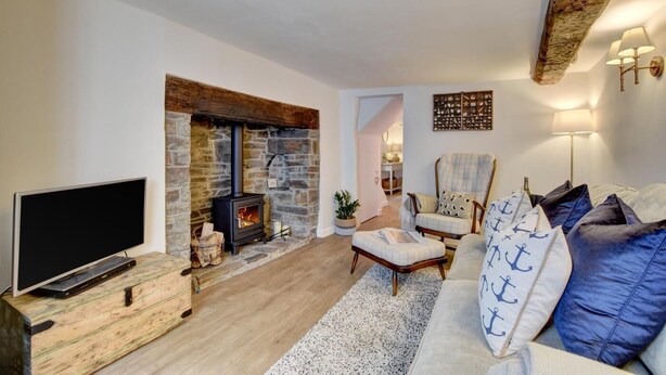 A living room with a stone fireplace, a television on a wooden stand, a sofa with nautical-themed pillows, and a chair. - 2 Bed in Appledore (oc-whimbc) (Appledore)
