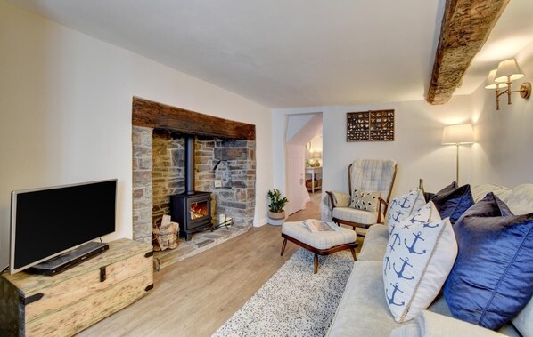 A living room with a stone fireplace, a television on a wooden stand, a sofa with nautical-themed pillows, and a chair.