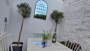 A white table with a book and glasses, two potted plants, a window, and a white wall.