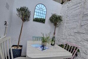 A white table with a book and glasses, two potted plants, a window, and a white wall.