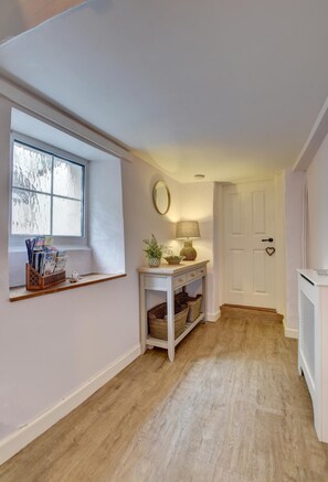 A hallway with a window, a console table with a lamp, wicker baskets, and a white door with a heart-shaped decoration.