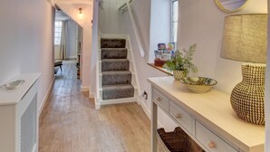 A hallway with a staircase, a radiator, a lamp, and baskets. - 2 Bed in Appledore (oc-whimbc) (Appledore)